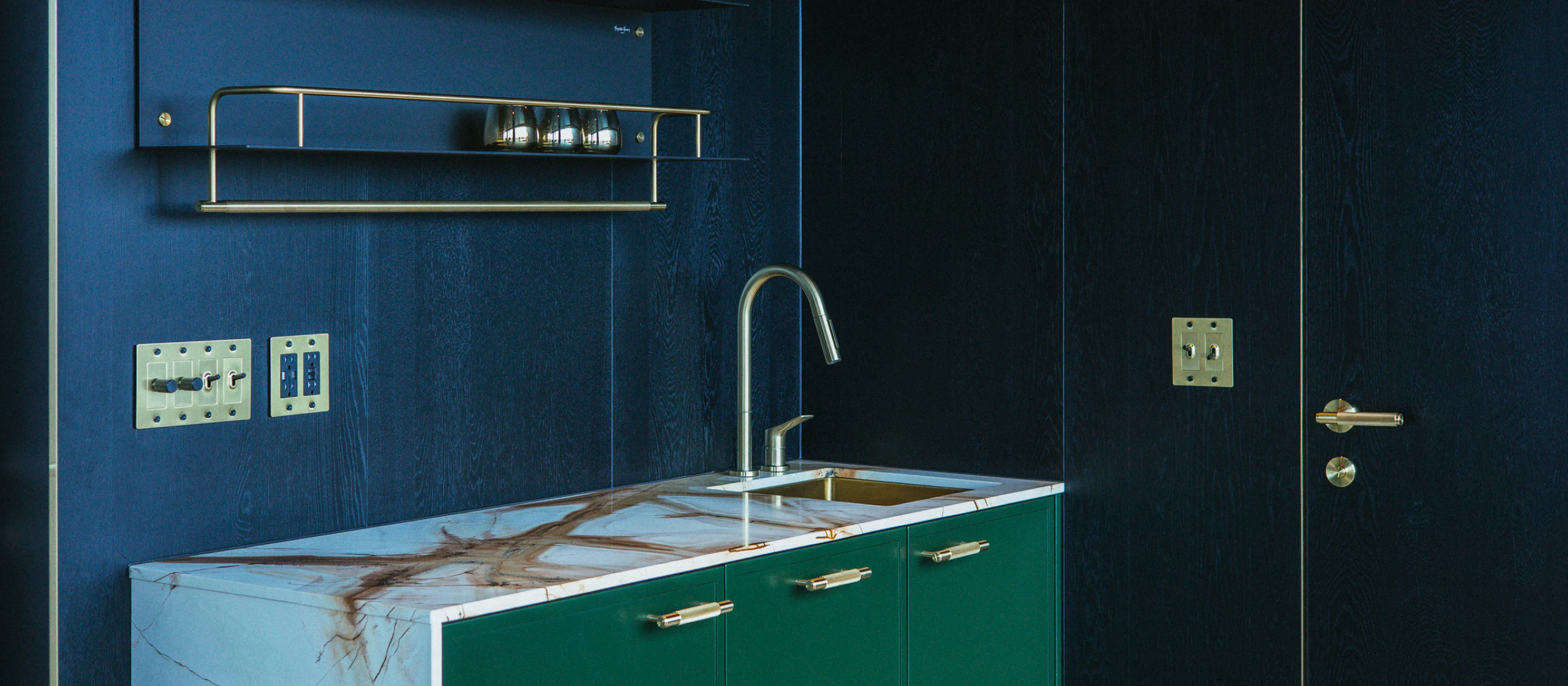 Compact kitchen with a veined marble counter, brass faucet, and forest-green cabinetry